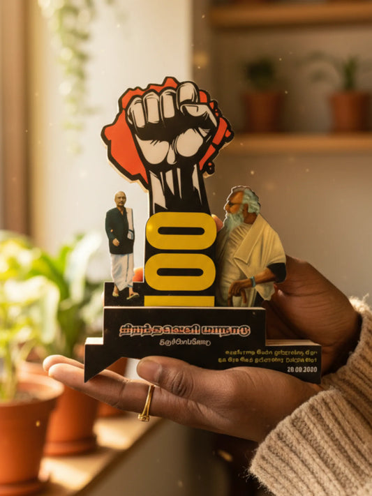 Hand holding a small statue with a raised fist and two figures, set against a blurred indoor background.