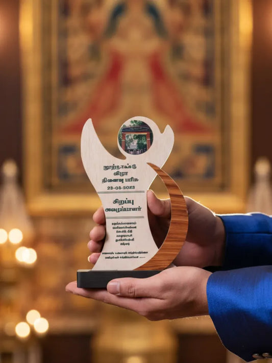 Hand holding a wooden award with text against a blurred background