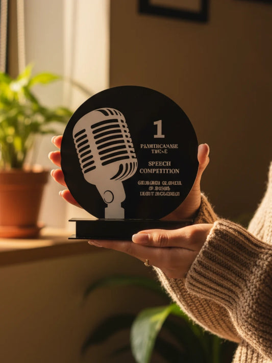 Hand holding a black and white award with a microphone design, indoors.