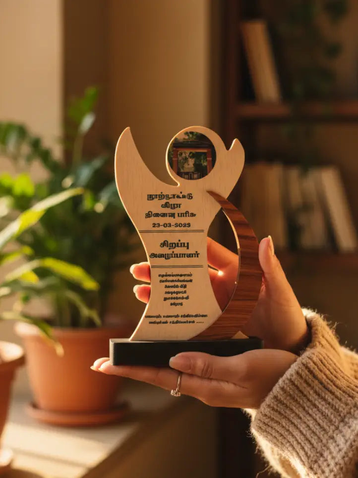 Hand holding a wooden award with text and design, blurred indoor background