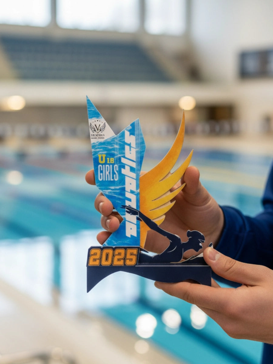 Person holding a swimming trophy with 'Girls' and '2025' on it in an indoor pool setting