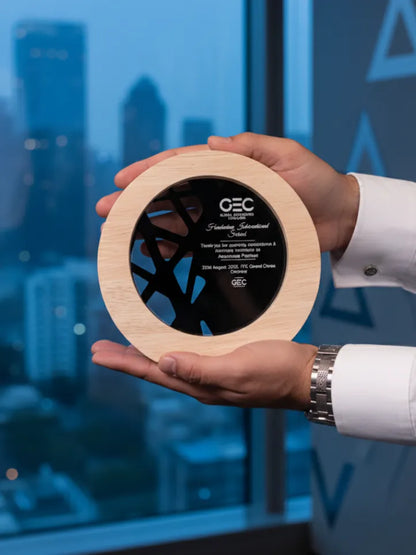 Person holding a wooden award with 'GEC' branding against a blurred cityscape background