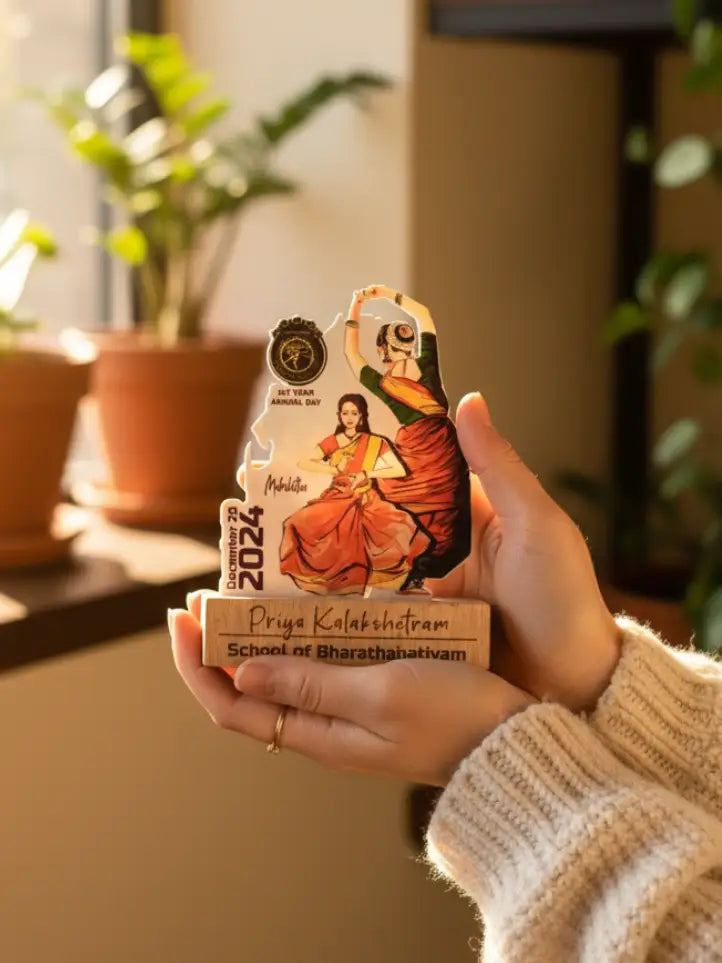 Hand holding a decorative item with artistic design and text, set against a blurred indoor background with plants.