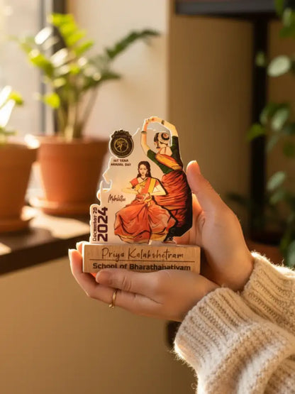 Hand holding a decorative item with artistic design and text, set against a blurred indoor background with plants.