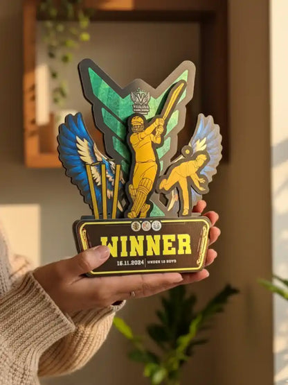 Hand holding a decorative plaque with 'Winner' text and colorful design against a neutral background