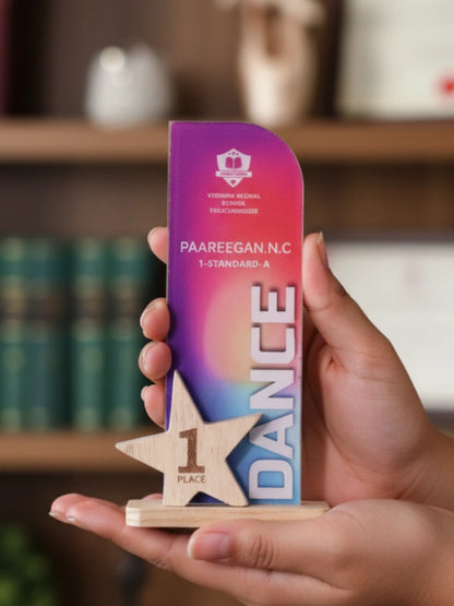 Hand holding a colorful trophy with 'Dance' and '1st Place' text against a blurred background
