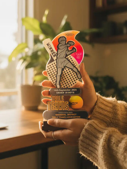Hand holding a table tennis trophy with a blurred indoor background