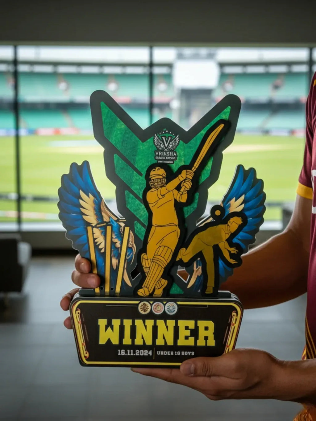Person holding a colorful trophy with 'Winner' text in front of a sports stadium.
