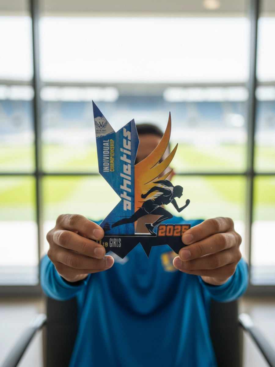 Person holding a blue and yellow award with 'athletics' text in front of a blurred indoor background