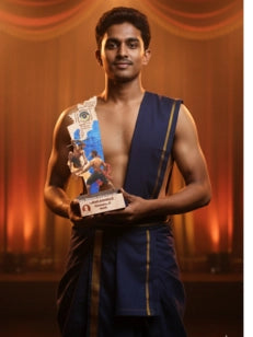 Man in traditional attire holding an award with a warm background