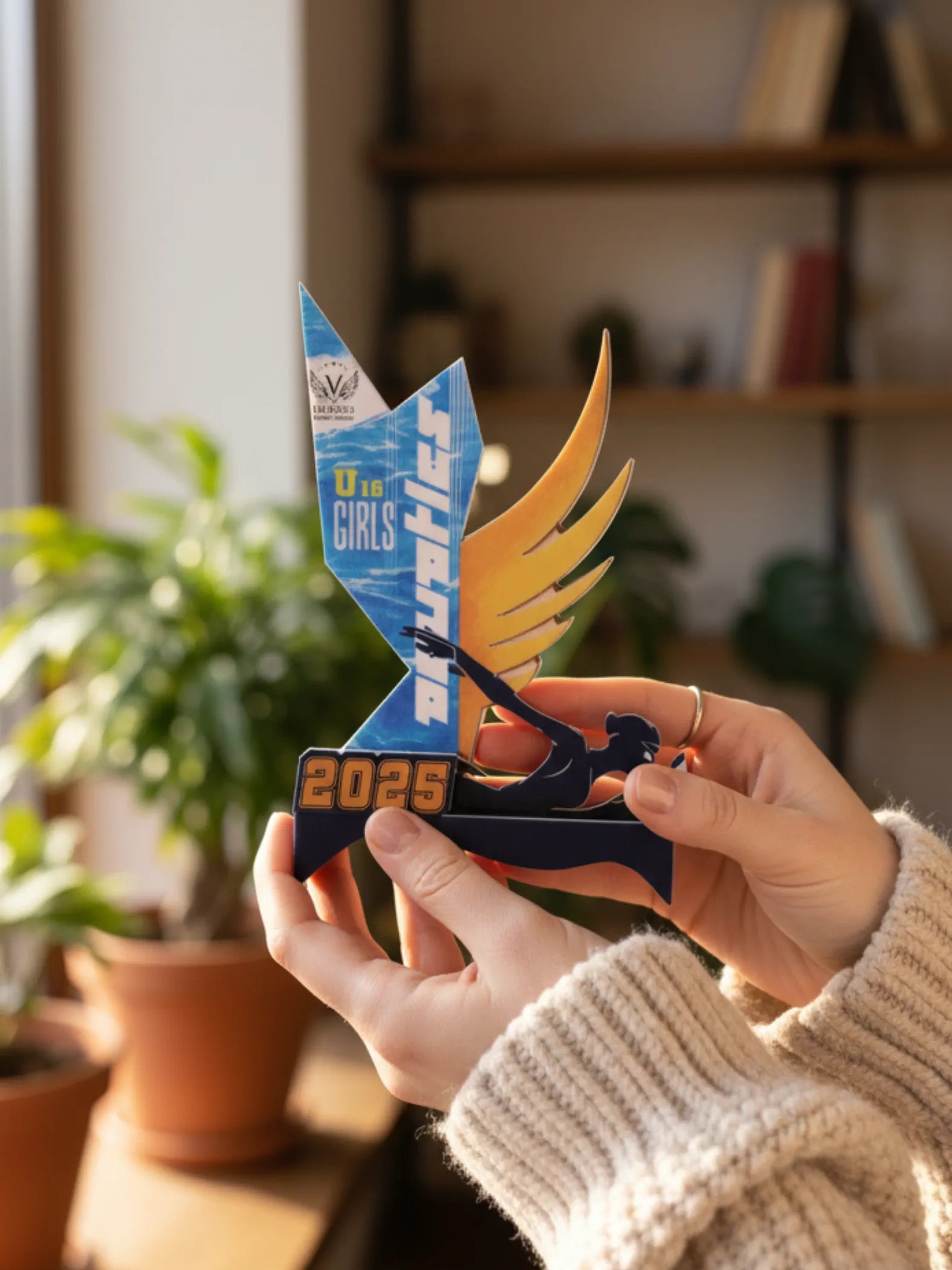 Person holding a blue and orange trophy with 'The Girls' and 'Sprinter' text in a home setting.