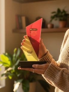 Person holding a red and yellow award in a home setting with plants and books.