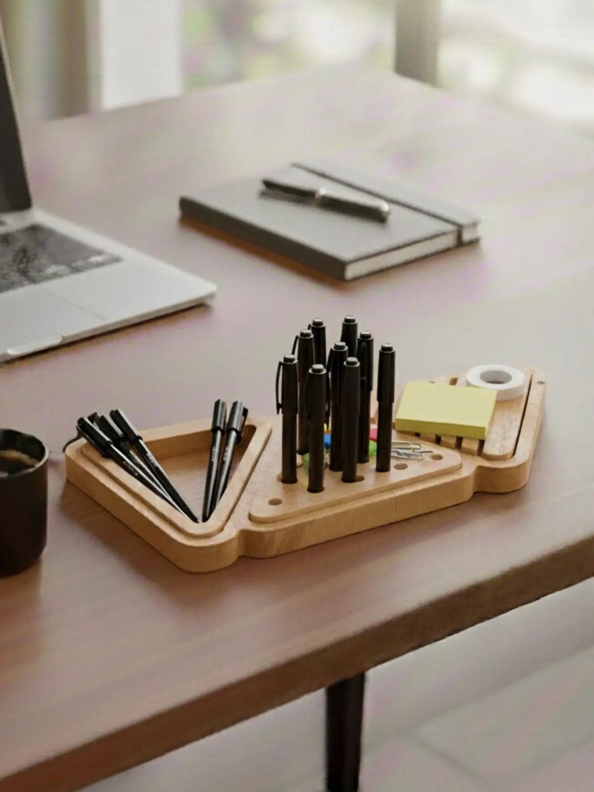 Wooden desk organizer with pens and a notebook on a desk.