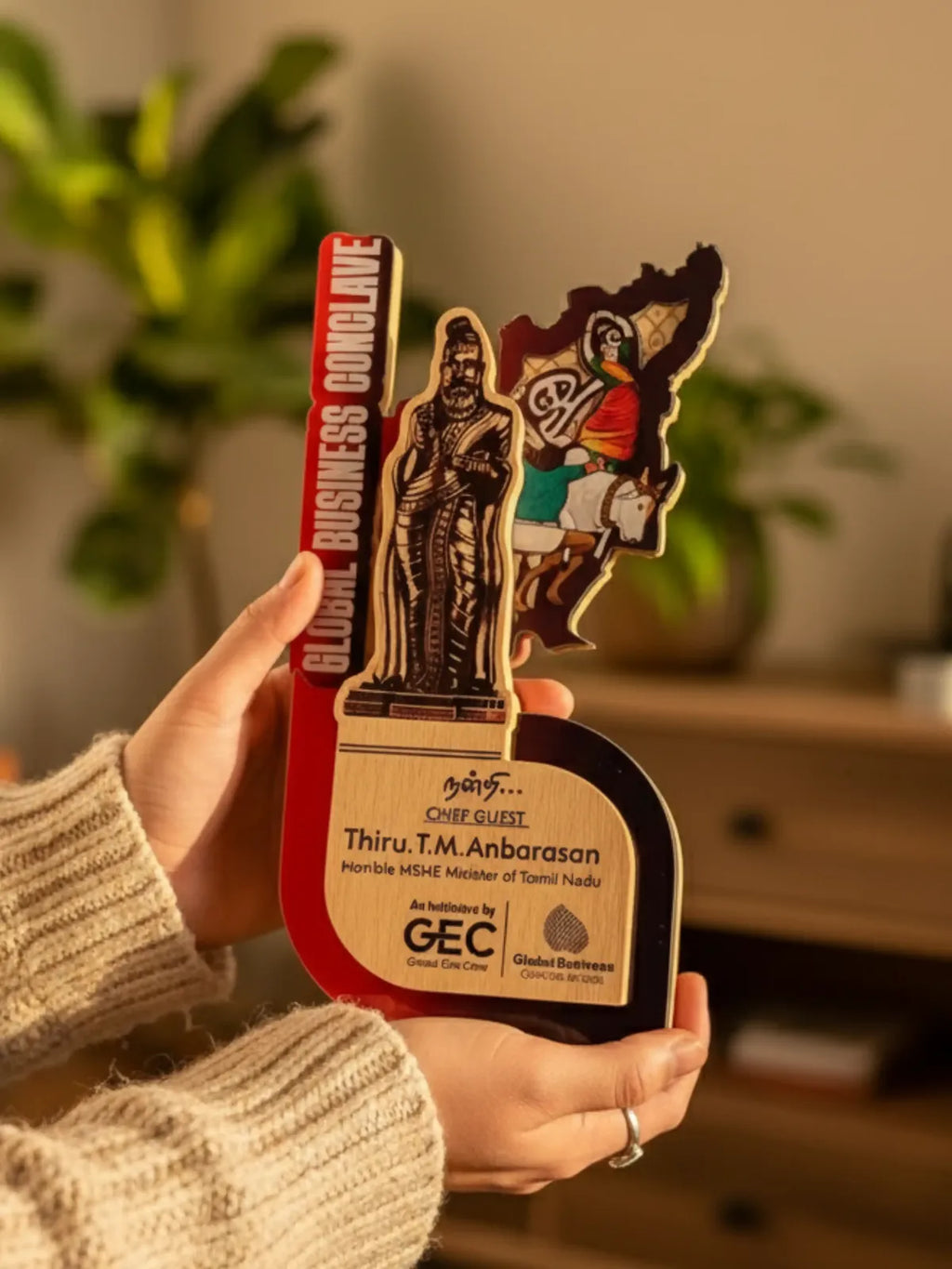 Hand holding a decorative item with statues and text, blurred indoor background