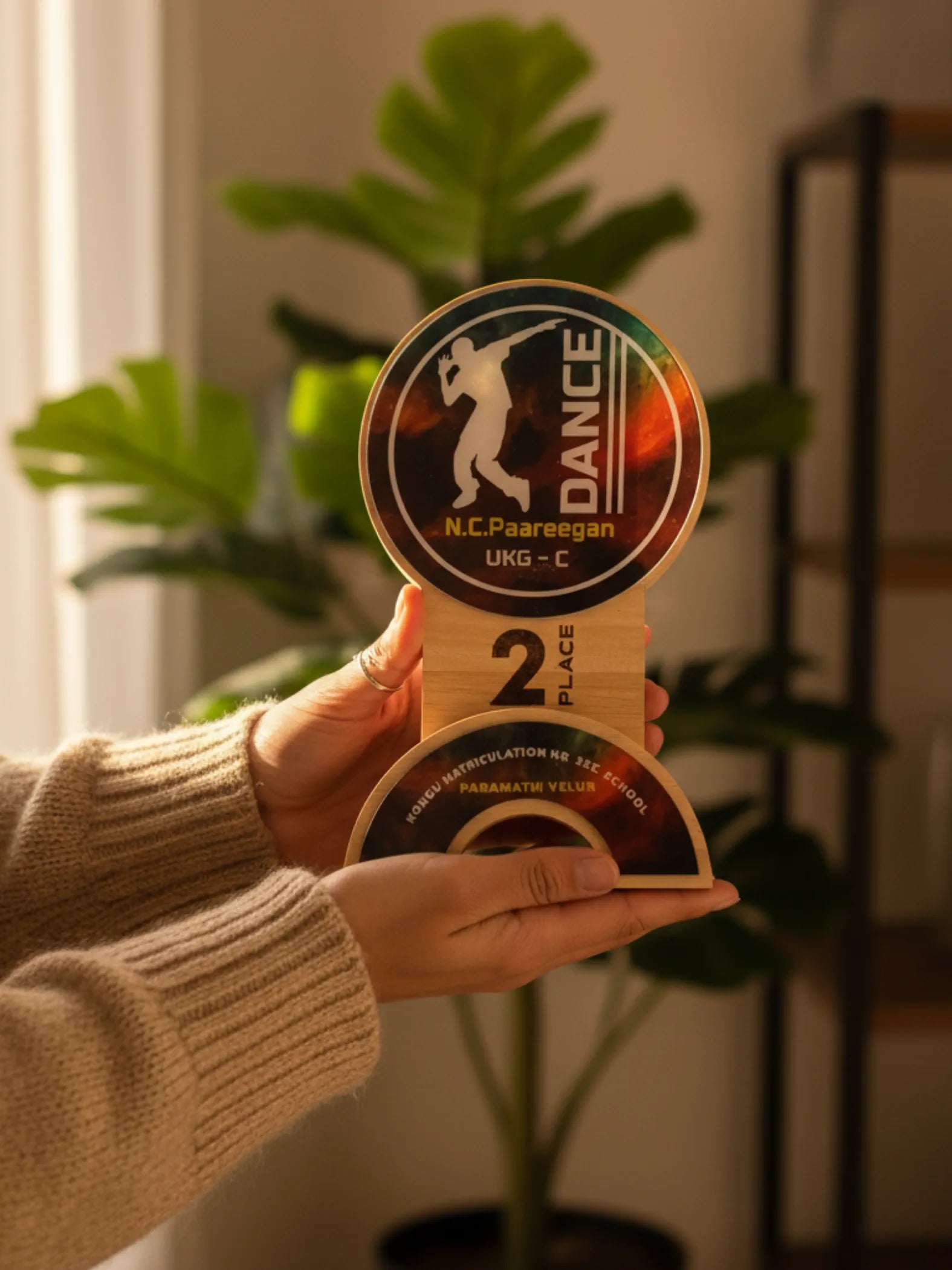 Hand holding a dance competition trophy with 'N.C. Paareegan' branding