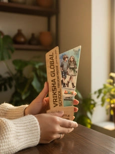 Person holding two books titled 'Vrikshaa Global' on a wooden table with a blurred indoor background.