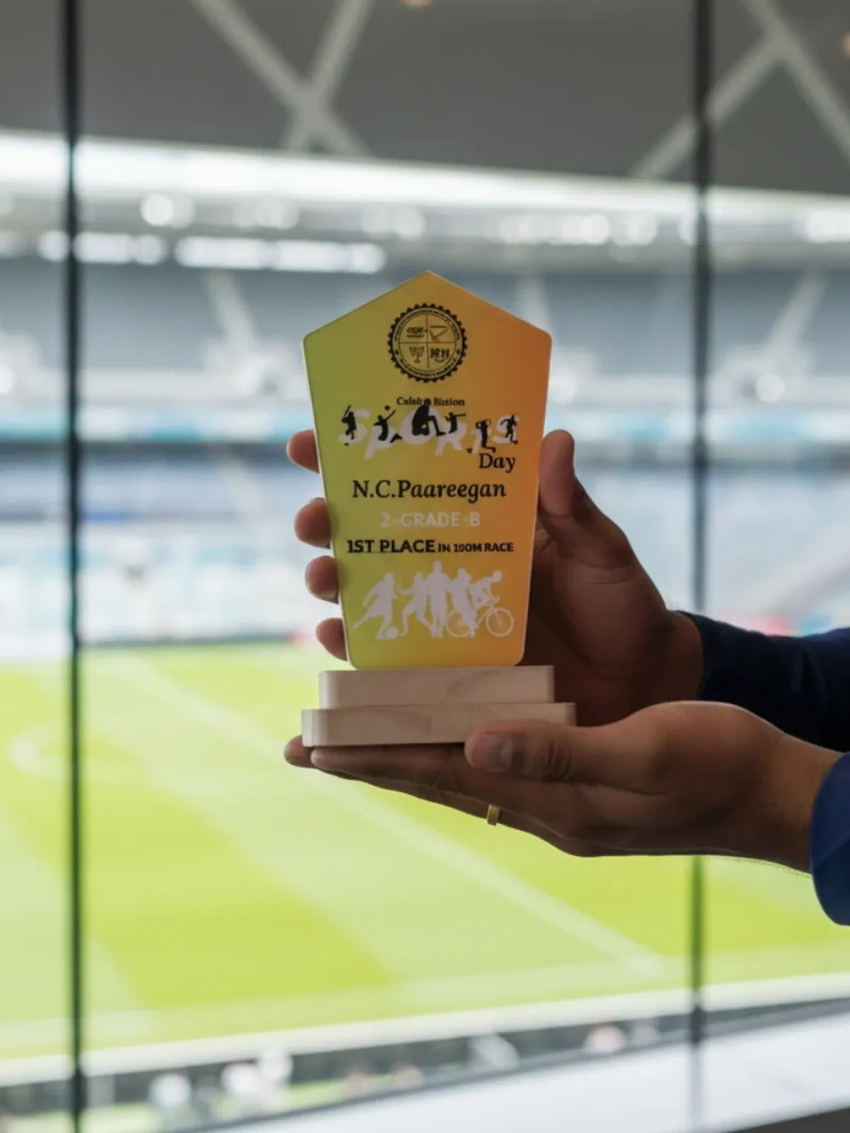 Hand holding a yellow award with text and graphics, blurred stadium background
