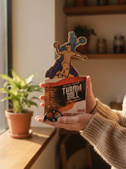 Person holding a 'Throw Ball' product packaging with a decorative design in a home setting.