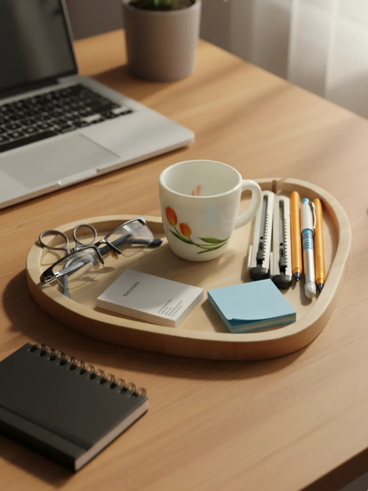 Wooden tray with office supplies including a mug, pens, and glasses on a desk.