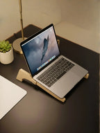 Laptop on a wooden stand on a desk with a plant and lamp in the background