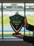 Person holding a trophy with 'RACE 100M' on it in front of a sports field.