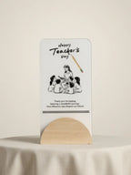 Card with illustration of children and teacher, text 'Happy Teacher's Day', on a stand against a beige background.
