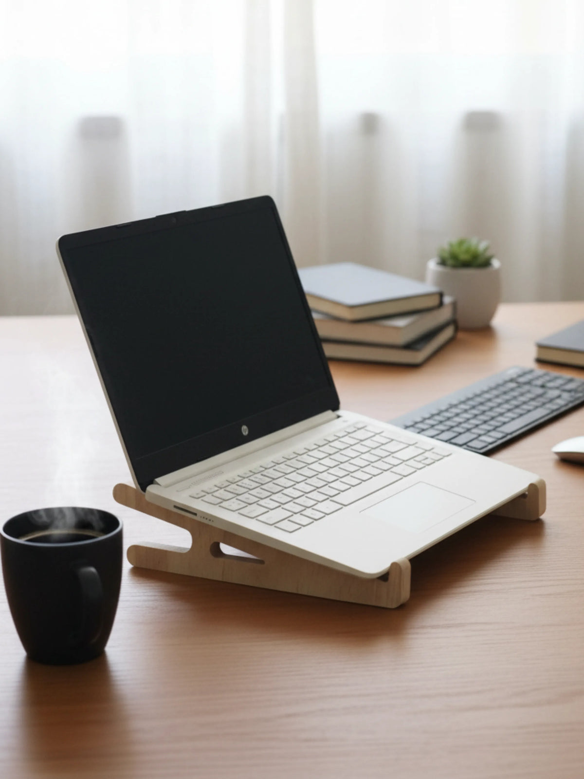 Laptop on a wooden stand on a desk with books and a plant in the background