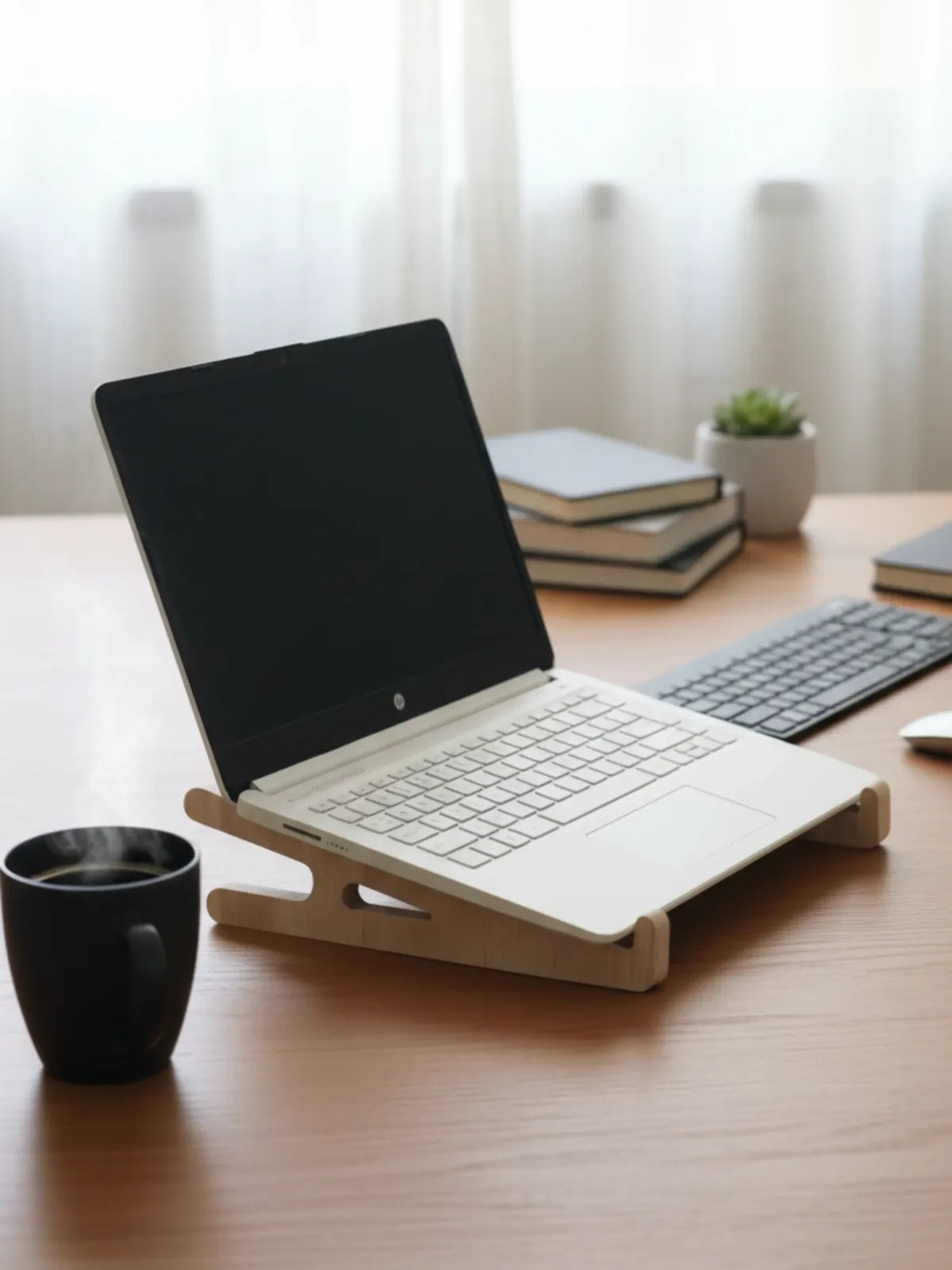 Laptop on a wooden stand on a desk with books and a plant in the background