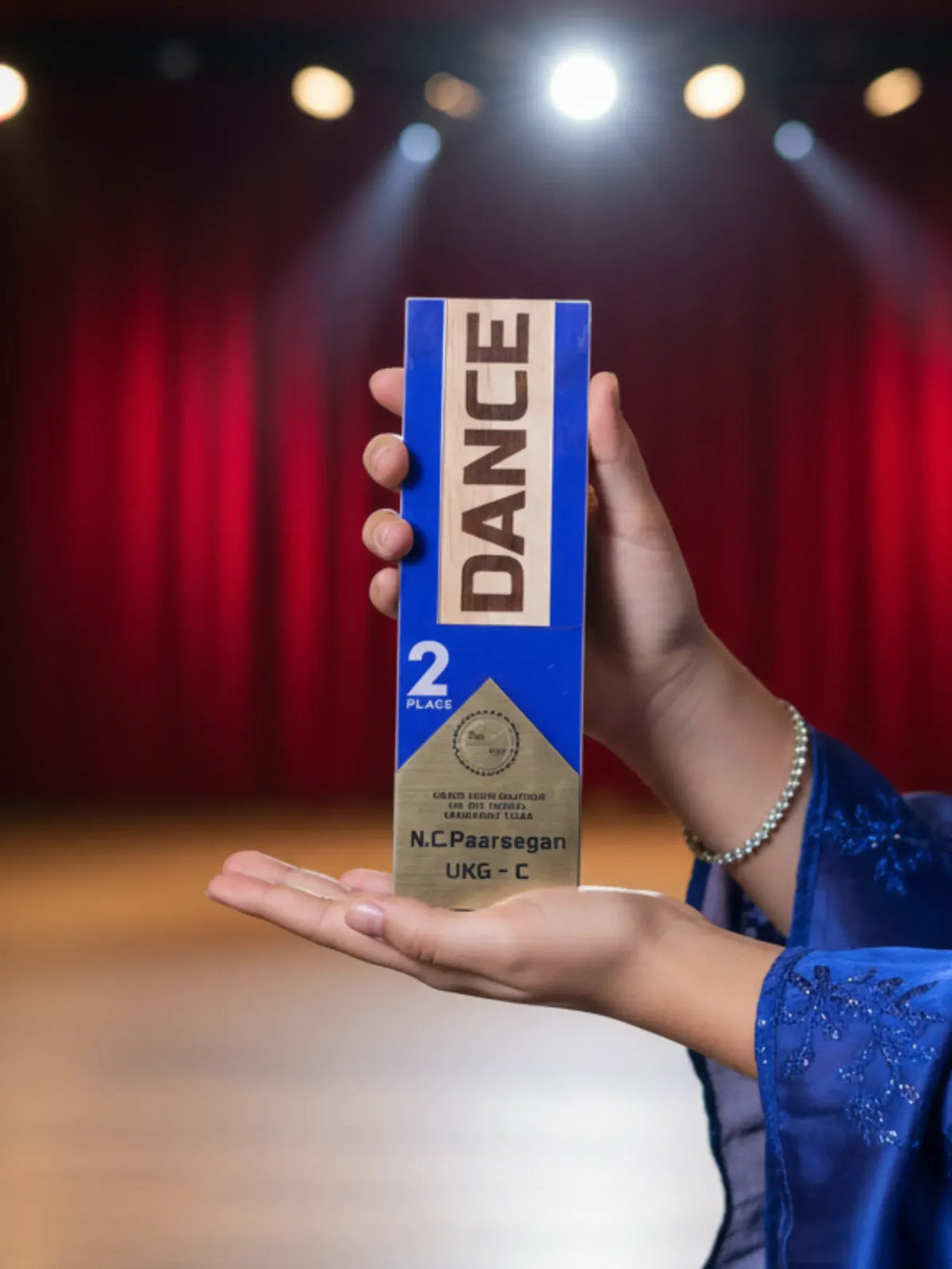 Person holding a 'DANCE' product box on a stage with red curtains and spotlights.