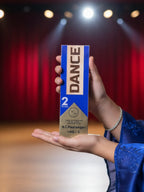Person holding a 'DANCE' product box on a stage with red curtains and spotlights.