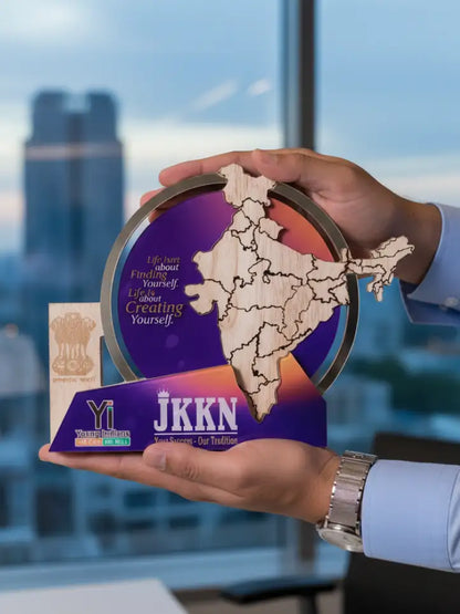 Hand holding a decorative item with 'YI' and 'JKKN' branding against a blurred cityscape background