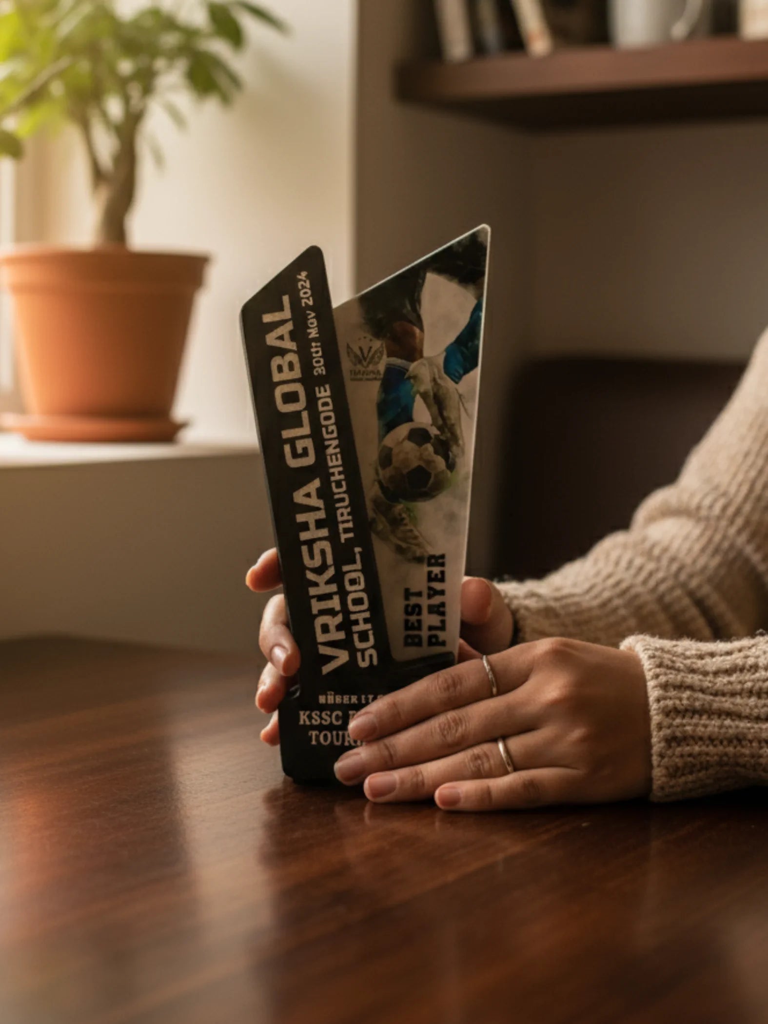 Person holding a Vriksha Global School book on a wooden table with a blurred background
