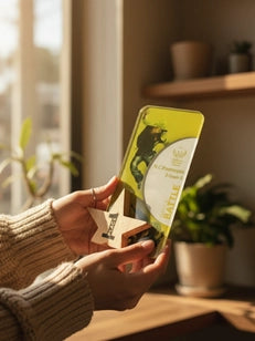 Person holding a green and white package in a home setting with plants and a window.