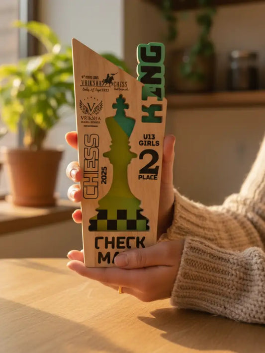 Person holding a wooden chess trophy with green and brown design, placed on a wooden surface.