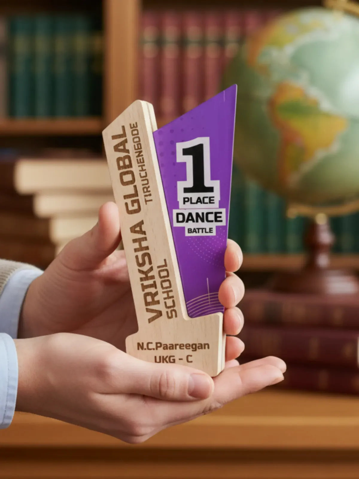 Hand holding a dance competition trophy with a bookshelf and globe in the background