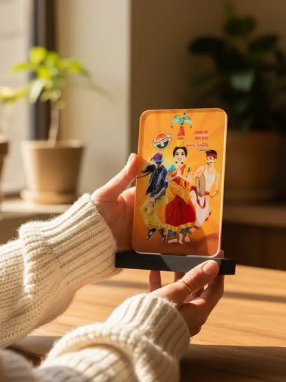 Person holding a phone case with colorful design of three people in traditional attire, indoor setting with plants.