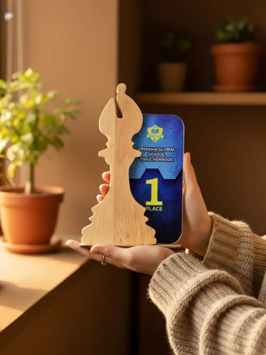 Person holding a smartphone with a blue case featuring a trophy design, next to a wooden chess piece on a wooden surface.