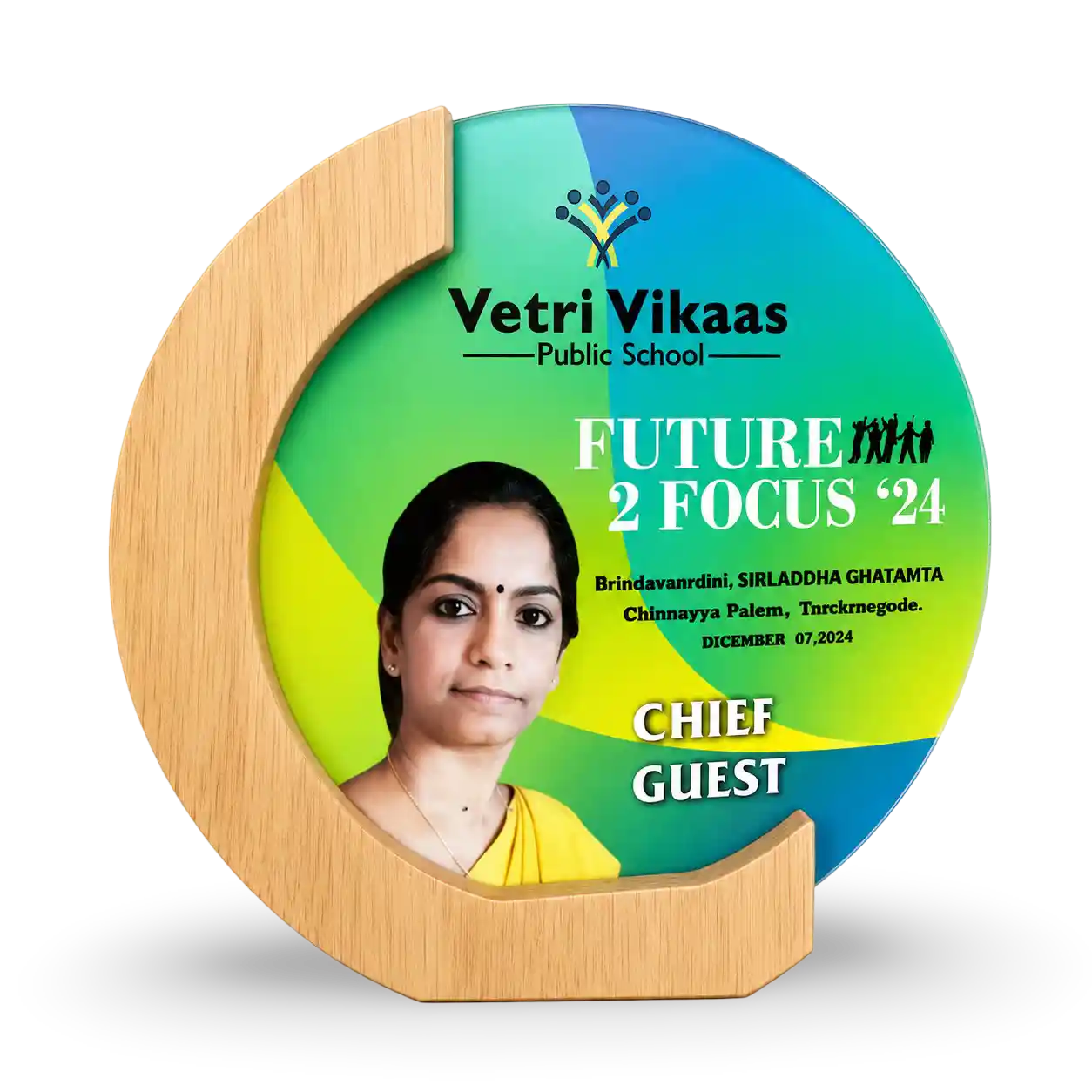 Round green and blue plaque with a wooden border featuring a photo of a woman and text about Vetri Vikaas Public School.