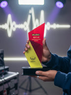 Person holding a red and yellow trophy with 'Music Battle' text against a blurred background
